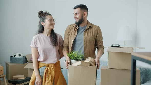 Portrait of Husband and Wife Holding House Keys and Cardboard Box Smiling in New Modern Apartment alt