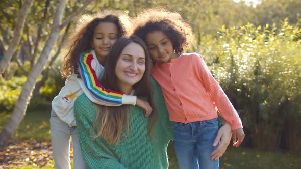 Caucasian Young Mom and Afro Daughters Hugging in Park alt