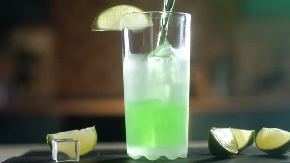 Carbonated green drink is slowly poured into a frozen glass with large ice cubes alt