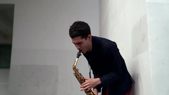 Street Musician Is Playing Saxophone, Medium Shot Against White Wall of Building alt