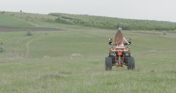 Free Woman Rides a Quad Near the Forest on a Plain of Green Grass alt