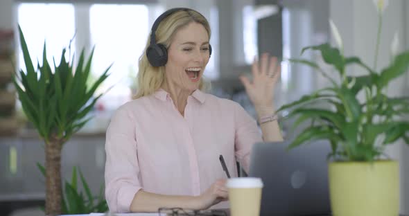 Blond woman with headphones making video call on laptop alt