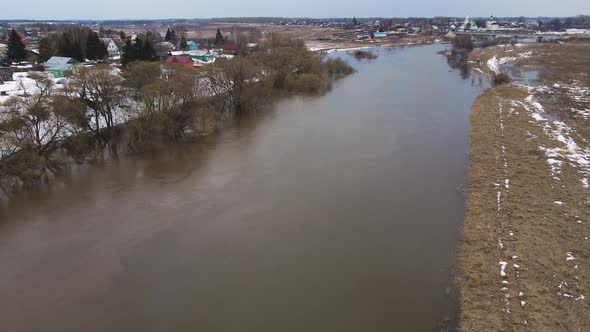 A Muddy River Stream with Gray Water the Remains of Snowdrifts on the Shore alt