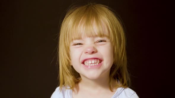 Studio portrait of a cute little blonde girl making excited, happy faces alt