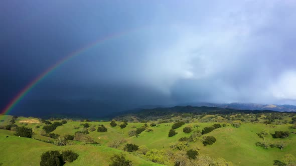 Farmland hills with cattle with beautiful double rainbow and mountains with snow and storm weather d alt