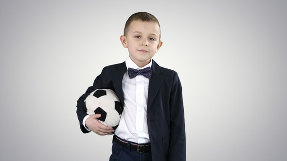 Happy young school boy holding a football on gradient background. alt