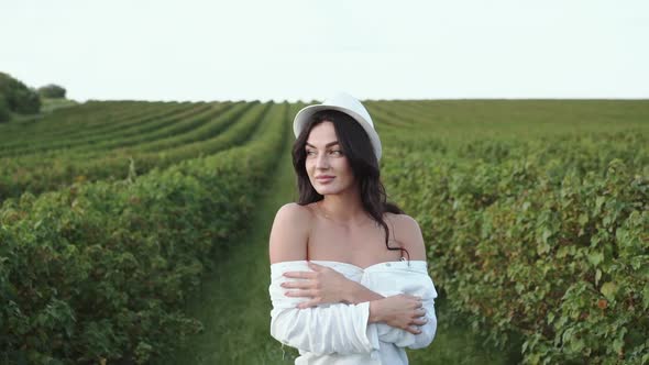 Pretty Brunette Walks Among Bush Plantation and Dreams with Smile on Face alt