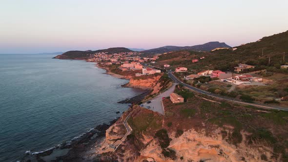 Aerial panoramic drone view of coastline and nearby village at sunset in Sardinia, Italy alt