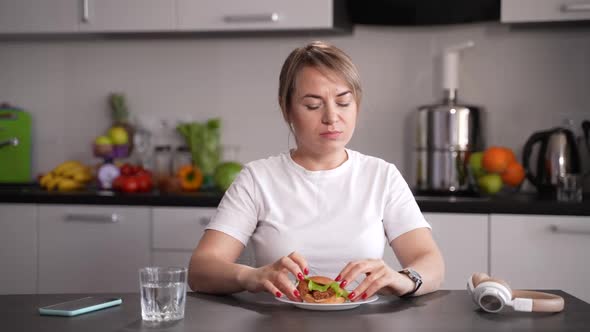 Slimming Woman Refusing to Eat Burger in Kitchen alt
