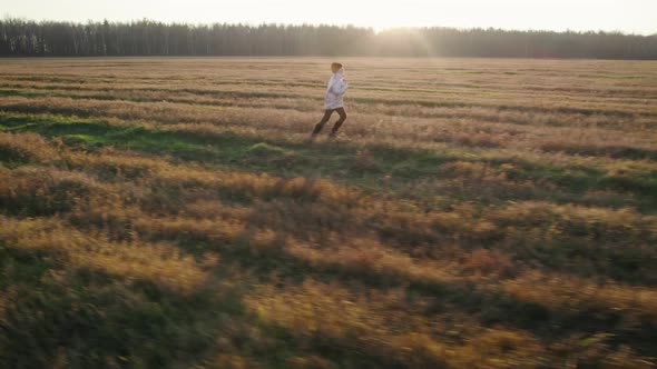 Teenage Girl Running Across the Field in Front of the Setting Sun alt