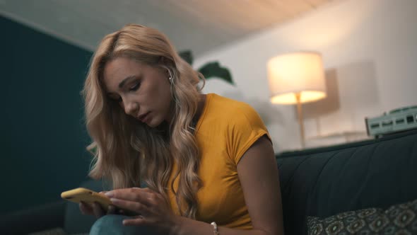 Woman in Bright Clothes Uses Smartphone While Sitting on the Couch alt