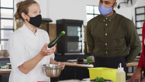 Caucasian female chef teaching diverse group wearing face masks alt