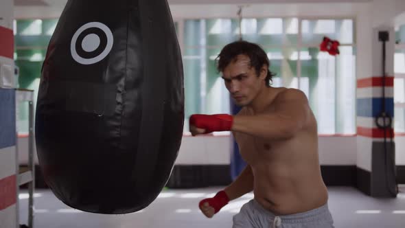 Caucasian man using punchbag in boxing gym alt