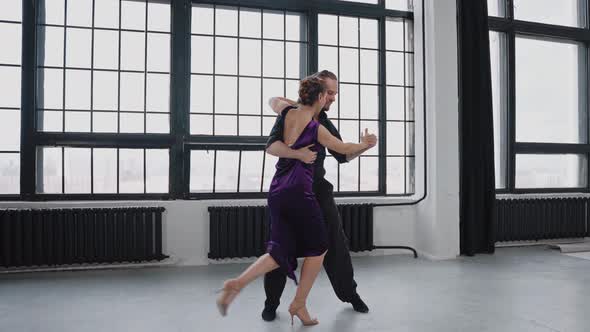 Full Growth Shot of a Pair Dancing Tango Against the Background of Large Windows