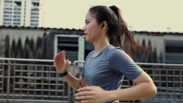 Runner Asian woman athlete wearing earphones listening to music running on the city.