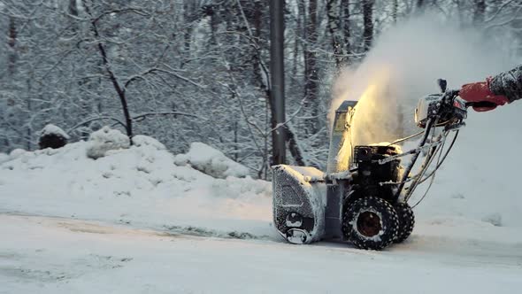 Snowcovered Man Cleans the Road in Winter with Blower Snow Removal Equipment