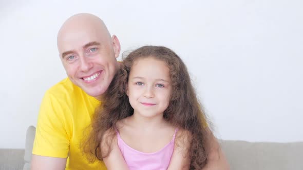 Happy Family, Loving Dad with a Small Daughter Are Sitting at Home on the Couch Looking at the alt