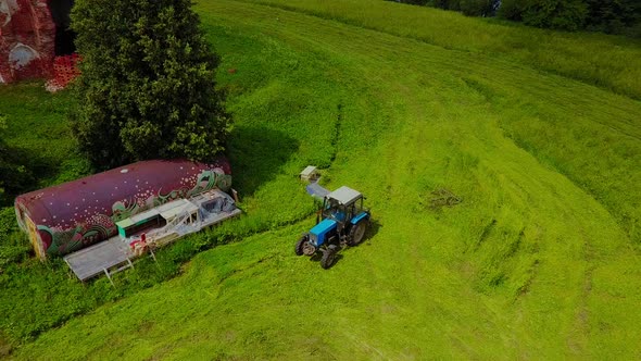 a Blue Tractor Mows the Grass at the Destroyed Church