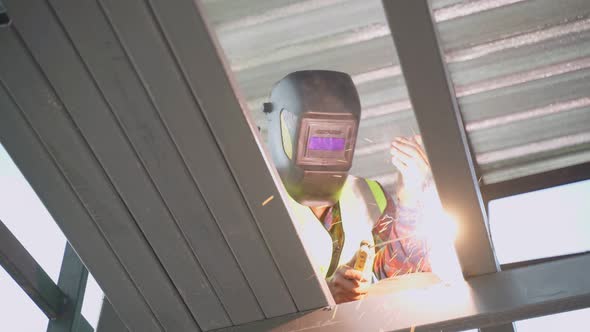 Asian construction builder male welder is welding steel beams in process of home renovation. alt