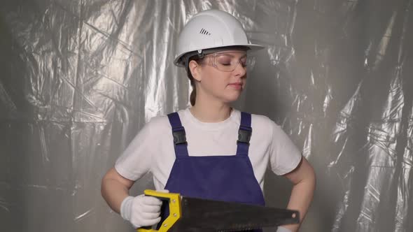 Woman Builder in Blue Overalls and White Hard Hat Helmet with Hand Saw