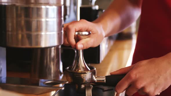 Waiter using a tamper to press ground coffee into a portafilter alt