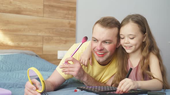 Portrait of Joyful Dad Looking at Result of Playing with Girl Having Facial Makeup