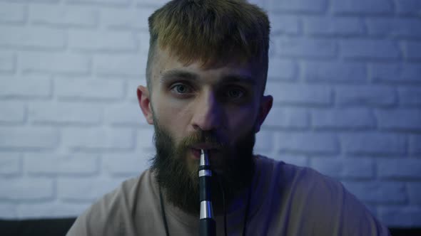 A Brutal Bearded Man Smokes a Hookah and Exhales Smoke alt