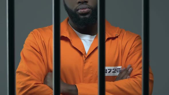 Black Criminal With Hands Crossed Standing in Prison Cell, Waiting for Judgment alt