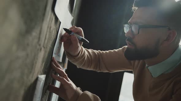 Bearded Man with Glasses Makes Notes on Blueprints on Loft-style Wall