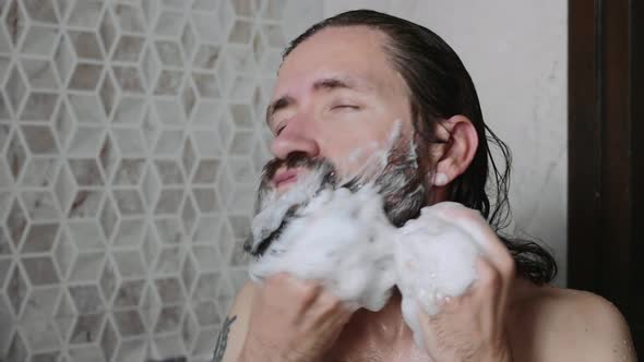 Man is Washing His Beard with Shampoo and Foam in the Shower