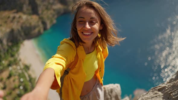 POV Happy Woman Hiker in Yellow Shirt Gives Hand to Her Teammate on Edge of Cliff on Mountain Top alt
