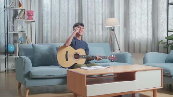 Asian Boy Composer With A Guitar Celebrating For Finishing Composing Music On Paper At Home alt