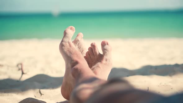 Man Lying On Beach And Moving Legs On Holiday Vacation. Happy Healthy Tourist Rest.Legs Man On Beach alt