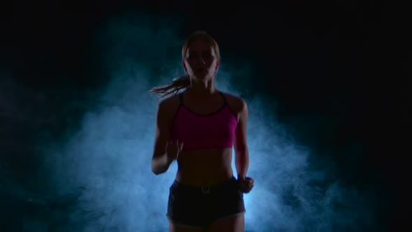 Girl Fitness Runs Steadily. Front View. Black Screen in the Smoke. Silhouette. Slow Motion. Close Up alt