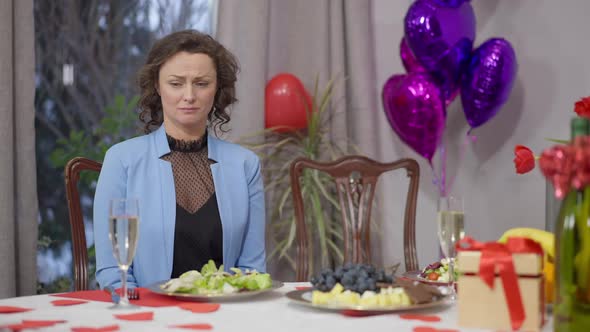 Portrait of Frustrated Crying Caucasian Woman Sitting at Valentine's Dinner Table Alone alt