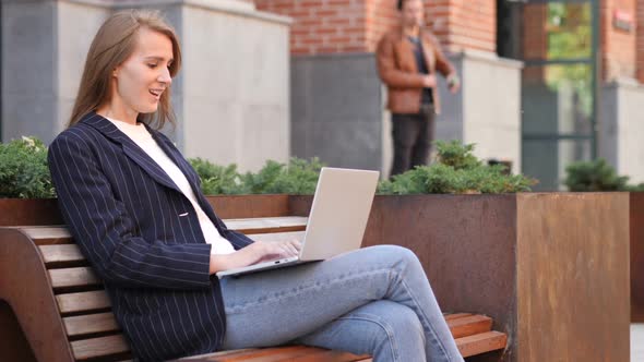 Excited Woman Celebrating Success on Laptop Sitting on Bench alt
