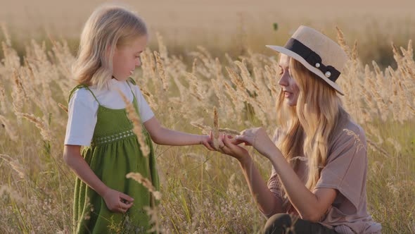 Caucasian Young Mother Woman in Hat Sits in Field with Little Girl Cute Daughter Child Holds Baby alt