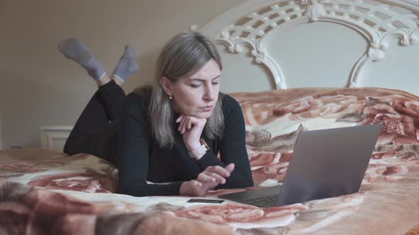 A Young Woman Lying on Her Bed is Browsing the Web on Her Laptop