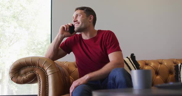 Happy caucasian man spending time at home and using smartphone alt