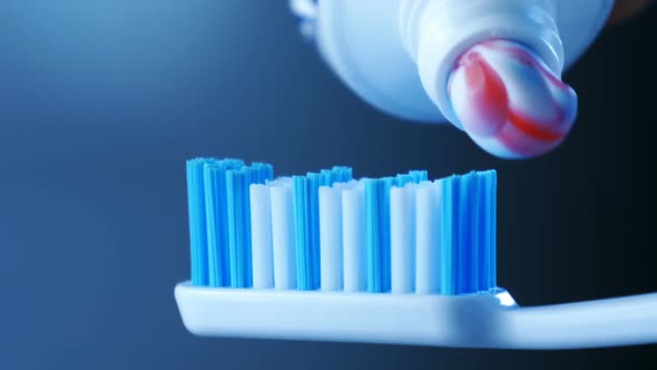 Dental Health - Squeezing Toothpaste with Colorful Stripes From a Tube Onto a Toothbrush.