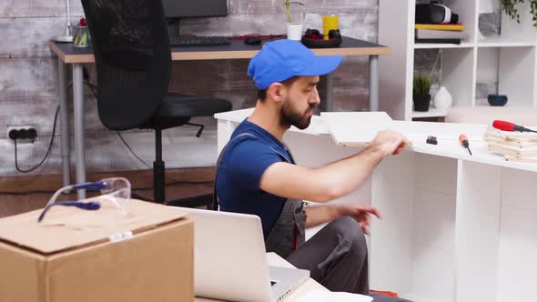 Male Worker Checking His Laptop After Mounting a Shelf alt