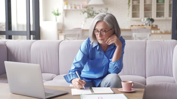 Middle Aged Woman Watching Webinar on Laptop Working From Home alt
