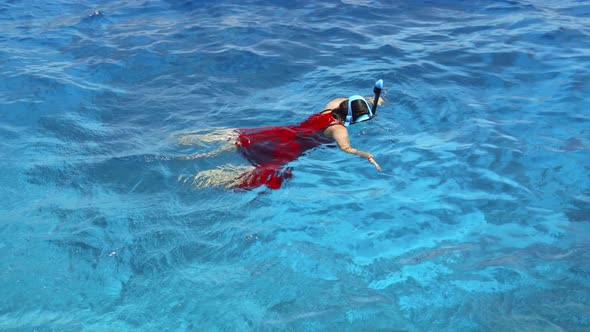 Unrecognizable girl bathes in a red dress on a clean sea surface.