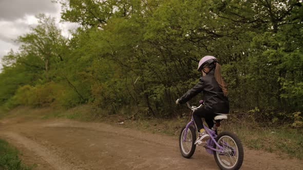 Cute Little Girl in Helmet Ride a Bicycle on Country Road Between White Hill and Forest. Steadycam