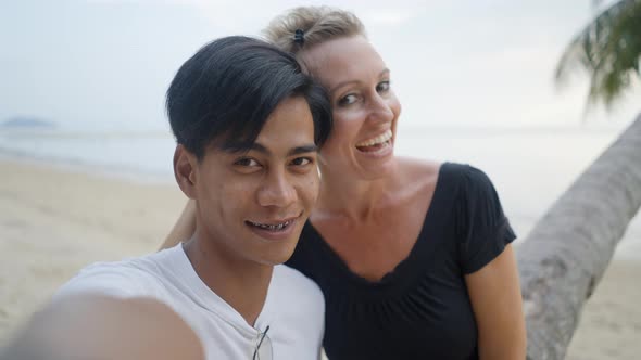 Happy Interracial Couple Dating on a Beach and Take a Selfie Video or Photo Kissing and Looking at alt