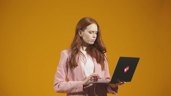 Redhaired Woman with a Laptop in Her Hands Stands on an Isolated Background in the Studio Smiling at