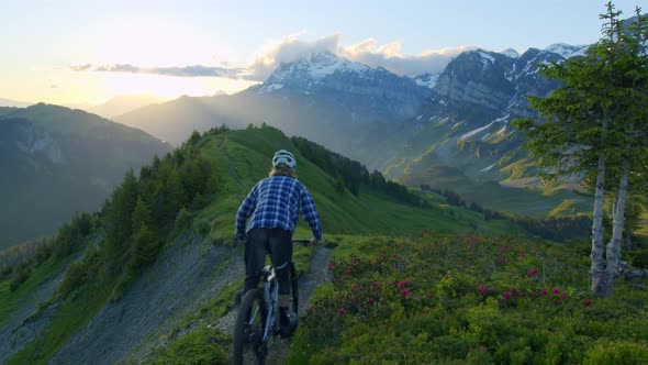 Mountain biker rides down an alpine ridge at sunrise alt