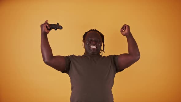 Excited African Man with Game Controler Isolated on Orange Background Happy As He Won the Game alt