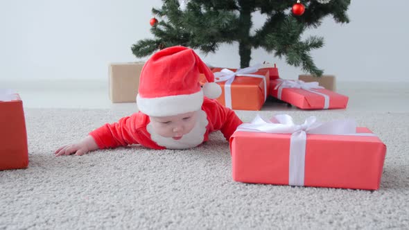 Christmas Concept. Cute Baby in Costume of Santa Claus, Looking a Gift alt