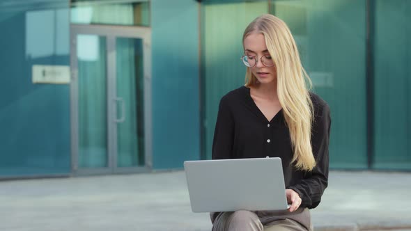 Pensive Millennial Woman in Glasses Look at Laptop Screen Outdoor Watching Online Conference or alt